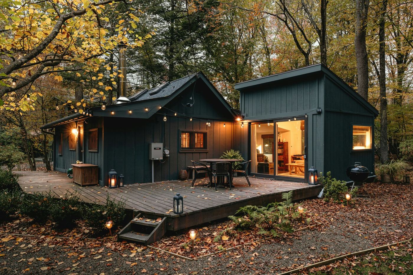 Dark-sided cabin with string lights and a deck among autumn trees at dusk